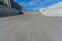 the empty parking lot in front of a wall with apartment buildings on it and a skateboarder on a ramp