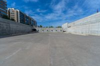 the empty parking lot in front of a wall with apartment buildings on it and a skateboarder on a ramp