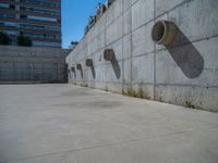 the empty parking lot in front of a wall with apartment buildings on it and a skateboarder on a ramp