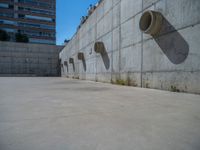 the empty parking lot in front of a wall with apartment buildings on it and a skateboarder on a ramp