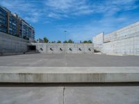 the empty parking lot in front of a wall with apartment buildings on it and a skateboarder on a ramp