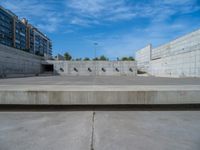 the empty parking lot in front of a wall with apartment buildings on it and a skateboarder on a ramp