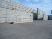 the empty parking lot in front of a wall with apartment buildings on it and a skateboarder on a ramp