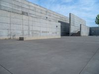 the empty parking lot in front of a wall with apartment buildings on it and a skateboarder on a ramp