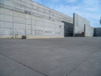 the empty parking lot in front of a wall with apartment buildings on it and a skateboarder on a ramp