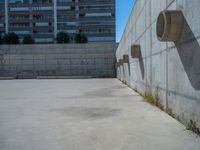 the empty parking lot in front of a wall with apartment buildings on it and a skateboarder on a ramp