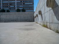 the empty parking lot in front of a wall with apartment buildings on it and a skateboarder on a ramp