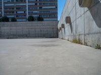 the empty parking lot in front of a wall with apartment buildings on it and a skateboarder on a ramp