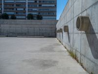 the empty parking lot in front of a wall with apartment buildings on it and a skateboarder on a ramp