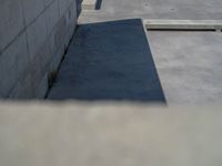 the empty parking lot in front of a wall with apartment buildings on it and a skateboarder on a ramp