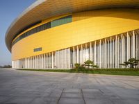 a modern looking yellow building with multiple layers of vertically shaped glass walls and green trees in front of it