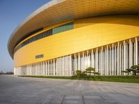 a modern looking yellow building with multiple layers of vertically shaped glass walls and green trees in front of it