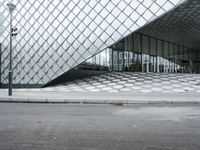 the empty street and sidewalk is lined with small circles of geometric shape, with a glass structure in the background