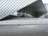 the empty street and sidewalk is lined with small circles of geometric shape, with a glass structure in the background
