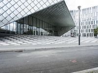 the empty street and sidewalk is lined with small circles of geometric shape, with a glass structure in the background