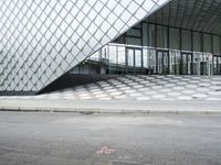 the empty street and sidewalk is lined with small circles of geometric shape, with a glass structure in the background