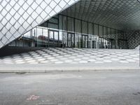 the empty street and sidewalk is lined with small circles of geometric shape, with a glass structure in the background