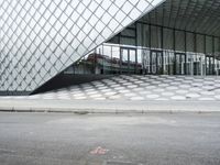 the empty street and sidewalk is lined with small circles of geometric shape, with a glass structure in the background