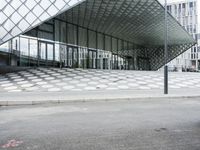 the empty street and sidewalk is lined with small circles of geometric shape, with a glass structure in the background