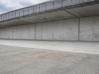 a skateboard sitting in an empty room under a bridge on a cloudy day at the edge of a parking lot