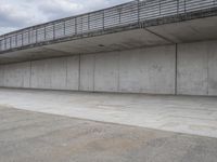 a skateboard sitting in an empty room under a bridge on a cloudy day at the edge of a parking lot