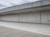 a skateboard sitting in an empty room under a bridge on a cloudy day at the edge of a parking lot