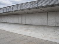 a skateboard sitting in an empty room under a bridge on a cloudy day at the edge of a parking lot