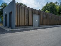 a metal building with a corrugated door in front of it and trees lining the street behind it