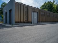 a metal building with a corrugated door in front of it and trees lining the street behind it