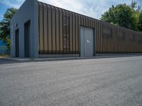 a metal building with a corrugated door in front of it and trees lining the street behind it