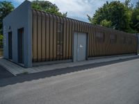 a metal building with a corrugated door in front of it and trees lining the street behind it