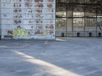 an empty, dilapidated parking area has lots of graffiti on the walls and doors of the building