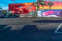 a mural with palm trees and other colorful designs painted on the wall behind a parked car