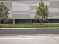 a gray building with two trees in front and a paved street in front of it