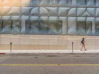 a woman walks by a large art installation near a city street corner with a traffic cone nearby