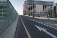 the road with arrow pointing towards an unfinished building on the side of it, in front of a fence and a concrete wall