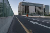 the road with arrow pointing towards an unfinished building on the side of it, in front of a fence and a concrete wall