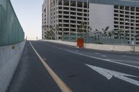 the road with arrow pointing towards an unfinished building on the side of it, in front of a fence and a concrete wall