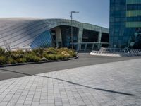 a paved road near large modern buildings and gardens in front of it with benches and plants