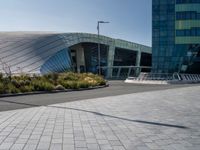 a paved road near large modern buildings and gardens in front of it with benches and plants