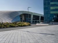 a paved road near large modern buildings and gardens in front of it with benches and plants