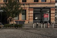 a picture of a building near a brick sidewalk and some fire hydrants with a red sign saying public space is open