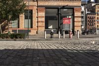 a picture of a building near a brick sidewalk and some fire hydrants with a red sign saying public space is open