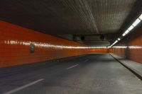 an empty city street with an orange painted wall and yellow lights on each side of the tunnel