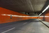 an empty city street with an orange painted wall and yellow lights on each side of the tunnel