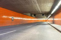 an empty city street with an orange painted wall and yellow lights on each side of the tunnel