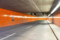 an empty city street with an orange painted wall and yellow lights on each side of the tunnel