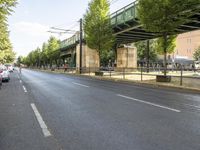 a very empty road on a sunny day with trees to side and overhead overpass