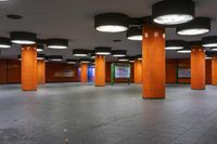 a public walkway with orange pillar covers in a building with brown and black pillars and tiled floor