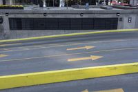 some yellow arrows are in the pavement pointing to left, and to right, on a sidewalk in front of some buildings